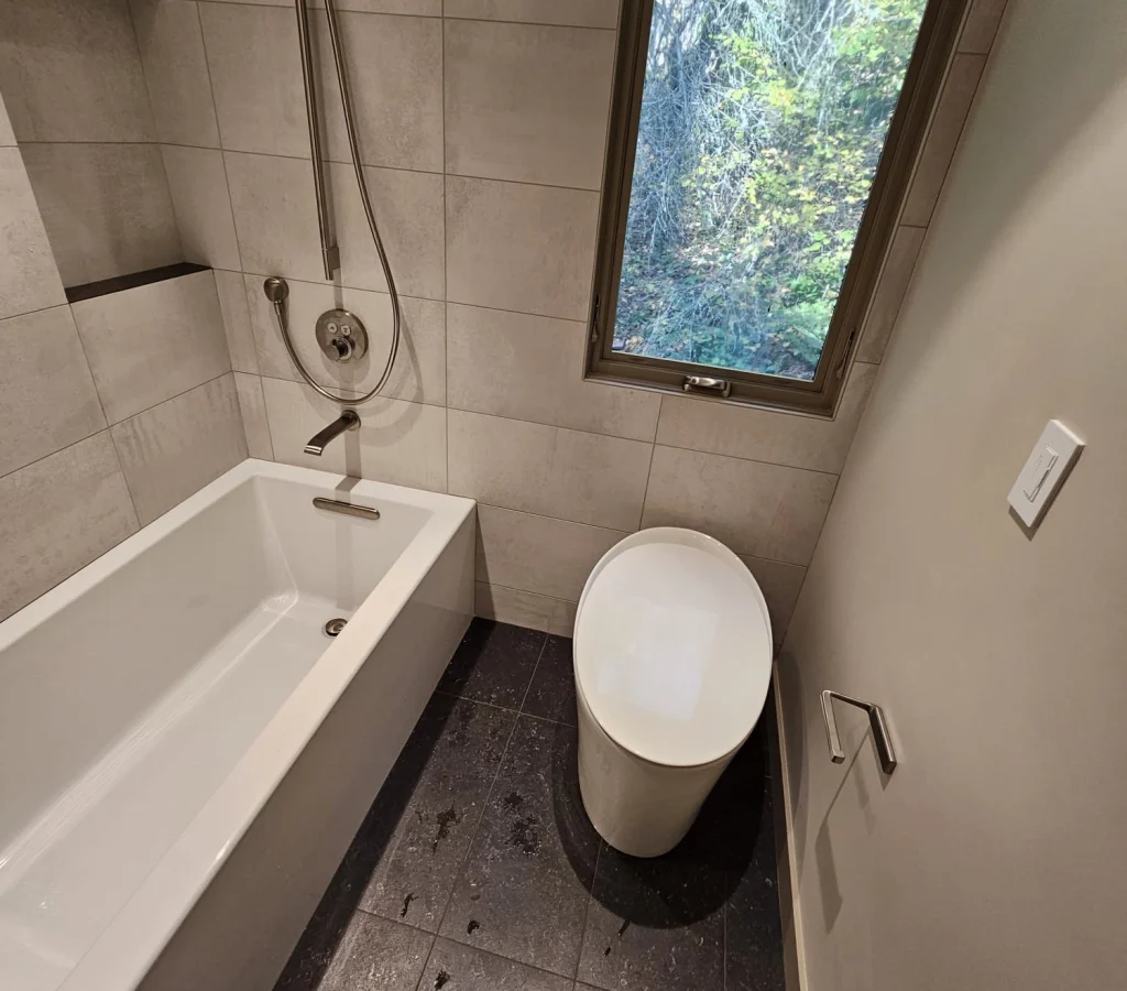 Small modern bathroom with a soaking tub, toilet, and a bright accent window